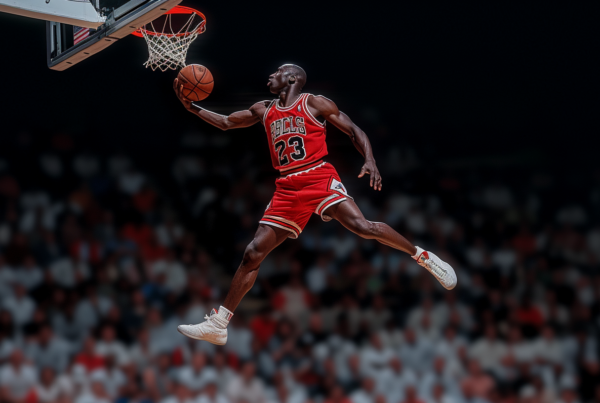 In this image, a man wearing a red uniform is seen mid-air, jumping up to dunk a basketball. He is focused and determined, with a basketball in his hand. The basketball player''s sneakers are visible, one pair in the foreground and another pair in the background. The player''s muscles are tense as he propels himself towards the hoop. The background is blurred, emphasizing the action happening in the foreground. The image captures the athleticism and skill of the basketball player as he executes a powerful dunk. The scene conveys the excitement and intensity of a basketball game moment.