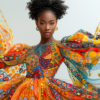 A young woman is standing confidently in the center of the image. She is wearing a stunning and vibrant colorful dress that flows gracefully around her. The dress is adorned with intricate patterns and designs, making it truly unique. She also has a matching scarf draped elegantly around her neck. The woman has a bright smile on her face, exuding joy and confidence. The background is blurred, highlighting her colorful attire. The woman''s age is estimated to be around 15 years old. Overall, she looks fashionable and stylish in her colorful ensemble