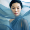 A young woman with a serene expression is captured in the image, wearing a beautiful blue dress that catches the eye. Her gaze is direct and engaging, as if she is looking straight at the camera. The woman''s face is partially covered by a delicate veil, adding an air of mystery and elegance to her appearance. The colors in the image are predominantly shades of blue and gray, creating a soothing and harmonious visual aesthetic. Overall, the scene conveys a sense of grace and sophistication, making it a captivating and intriguing portrait.