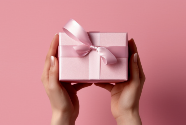 A woman is depicted holding a pink gift box adorned with a pink bow in the center. The gift box is shiny and wrapped in a satin material. The scene is set against a pink background, highlighting the vibrant colors of the gift box and bow. The person''s hand delicately holds the gift, showcasing a sense of care and excitement. The overall composition exudes a sense of joy and celebration, perfect for occasions like birthdays, anniversaries, or special events. The pink color scheme adds a feminine and elegant touch to the image, making it visually appealing and eye-catching.