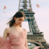 A beautiful young woman wearing a pink dress is striking a pose in front of the iconic Eiffel Tower in Paris. The woman is standing confidently, with the Eiffel Tower towering behind her. The scene is serene and picturesque, with the woman adding a touch of elegance to the already stunning backdrop. The pink dress complements the romantic ambiance of the setting, creating a lovely contrast against the steel structure of the Eiffel Tower. The woman''s posture exudes grace and poise, making her the focal point of the image against the backdrop of the famous landmark.