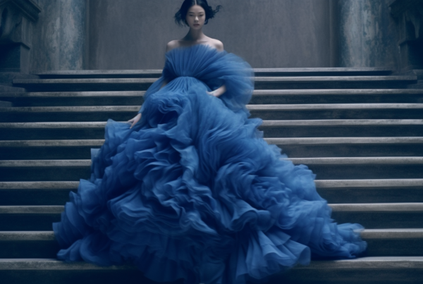 A young woman with long brown hair is seated gracefully on a grand staircase, wearing a stunning blue gown. The gown flows elegantly around her, creating a striking contrast against the neutral stone of the stairs. The woman exudes poise and elegance as she gazes off into the distance, lost in thought. The intricate details of the gown''s design are highlighted by the soft lighting, making it appear even more regal. The scene conveys a sense of beauty and sophistication, with the woman serving as a captivating focal point in this architectural setting.