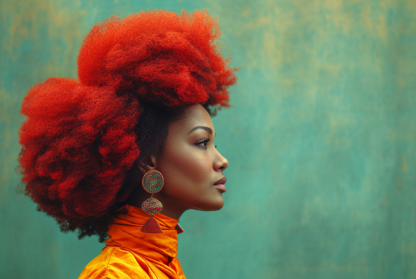 In this image, we see a woman with a striking and vibrant bright red afro hair. She is wearing a colorful dress and has a pair of earrings. The woman''s face is visible as she looks away from the camera. Additionally, there is a stuffed toy in the background. The colors in the image are primarily red, blue, and black. The woman''s red hair stands out as the focal point of the image. The overall composition suggests a sense of individuality and style. The woman''s unique hairstyle and colorful outfit make for a visually captivating scene.