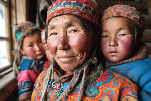 In this image, we see a woman wearing traditional clothing with two children on her back. One child is on her lap while the other is on her shoulders. The woman is wearing a red hat and a red scarf. The children are wrapped in colorful blankets. The woman has a smile on her face, and the children appear to be happy. The background shows a window and a remote control. The overall color scheme of the image includes shades of brown, blue, and white. The woman and children seem to be in a cozy and intimate setting.