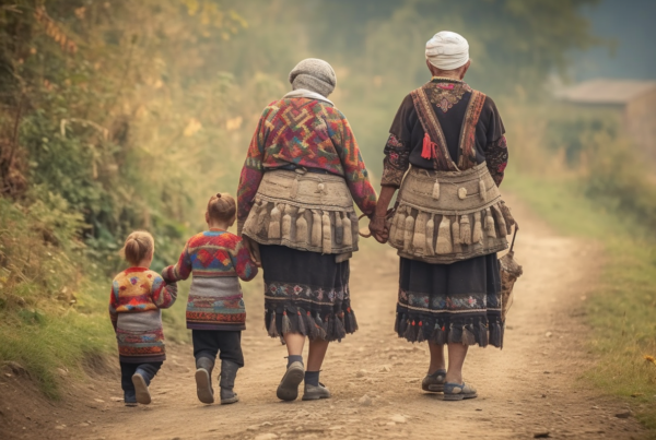 A woman and two children are walking down a dirt road in a rural setting. The woman is wearing a traditional dress, and one of the children is wearing sneakers while the other child is wearing boots. The woman is also accompanied by a horse in the background. The scene depicts a peaceful countryside setting with the group making their way along the path. The colors in the image are earthy tones, with the primary colors being shades of brown and beige. The overall atmosphere is serene and evokes a sense of simplicity and connection to nature.