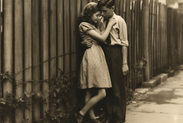 A sepia photograph captures a young couple standing next to a fence, embracing each other in a tender moment. The image is black and white, highlighting the couple''s love as they share a kiss. The woman is wearing a dress and the man is in a suit. The woman''s feet are visible in a pair of leather shoes. Additionally, there is a tie and a bracelet present in the image. The setting appears to be in a city, with a window visible in the background. The overall tone of the image is nostalgic and romantic.
